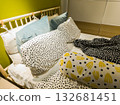 Cozy bedroom interior with colorful pillows and patterned bedding on an unmade bed. Modern home design with playful polka dots and bright yellow accents creating a cheerful, relaxed atmosphere. 132681451