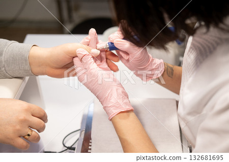 Manicure treatment. Spa therapy. Beauty female technician hands in pink medical gloves using brush preparing clients nail fingers for professional process. Manicure treatment. Spa therapy. Beauty female technician hands in pink medical gloves using brush preparing clients nail fingers for professional process. 132681695