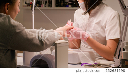 Manicure process. Polygel technique. Female beautician hands in latex gloves mask drawing varnish on clients nail tip with thin brush salon routine. 132681698