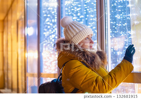 Young woman in winter clothes looks at shiny store window. Christmas shopping and sales. Young woman in winter clothes looks at shiny store window. Christmas shopping and sales. 132681915