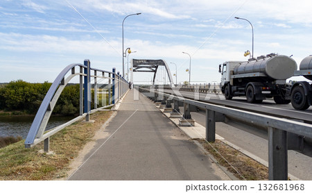 Milk tanker with a tank trailer travels along a highway over a bridge over a river. Concept for delivering milk from dairy farms Milk tanker with a tank trailer travels along a highway over a bridge over a river. Concept for delivering milk from dairy farms 132681968