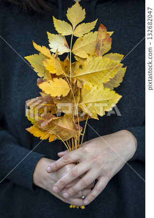 Woman holding a bouquet of yellow autumn leaves, capturing the warmth and beauty of fall. Autumn Mood with Yellow Leaves 132682047