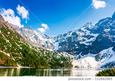mountain lake in tatra national park. morskie oko surrounded with rugged snow capped peaks in early spring. beautiful view of reflection and ice on water. green environment background under blue sky 132682063