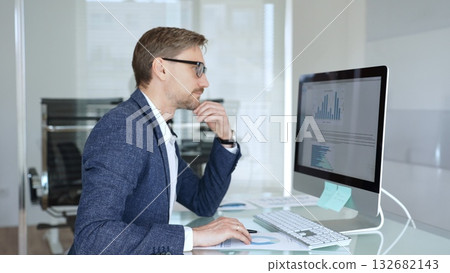 Businessman in a blue jacket analyzing financial data charts on computer, making important business decisions in modern office. Business people concept Businessman in a blue jacket analyzing financial data charts on computer, making important business decisions in modern office. Business people concept 132682143