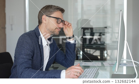 Professional businessman in a blue jacket working on desktop computer in modern office, focusing on his work and business tasks. Business people concept Professional businessman in a blue jacket working on desktop computer in modern office, focusing on his work and business tasks. Business people concept 132682144