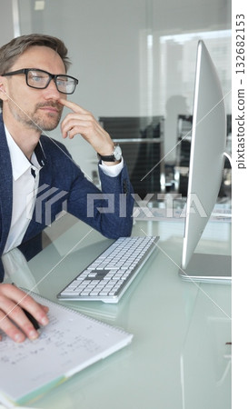Businessman in a blue jacket thinking and brainstorming ideas while working on computer and taking notes in modern office. Business people concept Businessman in a blue jacket thinking and brainstorming ideas while working on computer and taking notes in modern office. Business people concept 132682153