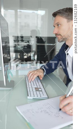 Professional businessman in a blue jacket working on desktop computer in modern office, focusing on his work and business tasks. Business people concept Professional businessman in a blue jacket working on desktop computer in modern office, focusing on his work and business tasks. Business people concept 132682189
