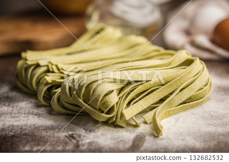 Green tagliatelle pasta on kitchen table. 132682532