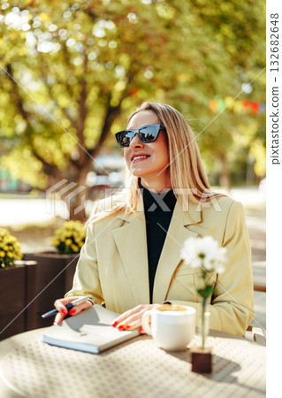 Woman enjoying a sunny day at a cafe while writing notes outdoors Woman enjoying a sunny day at a cafe while writing notes outdoors 132682648