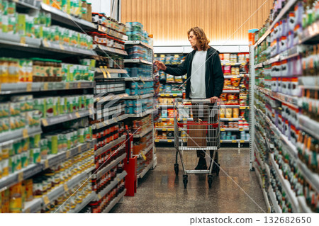 Shopping in a grocery store aisle with a cart full of canned goods 132682650