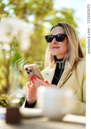 Woman enjoying a sunny day outdoors while using her smartphone at a cafe 132682655