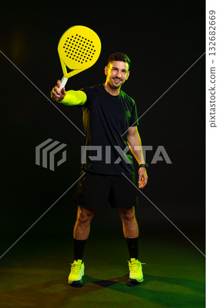 Young man holding a bright yellow paddle in a dark studio setting Young man holding a bright yellow paddle in a dark studio setting 132682669