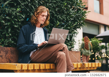 Young man working on laptop outside at a cafe during a sunny afternoon 132682671