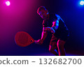 Man plays paddle tennis under colorful lights in a dark setting during a lively match 132682700
