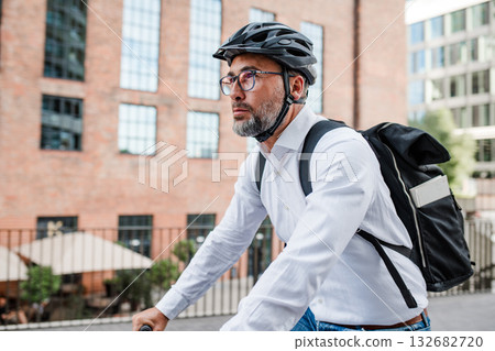 Man riding bike to work in city with helmet and backpack Man riding bike to work in city with helmet and backpack 132682720