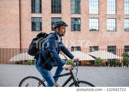 Man riding bike to work in city with helmet and backpack Man riding bike to work in city with helmet and backpack 132682722