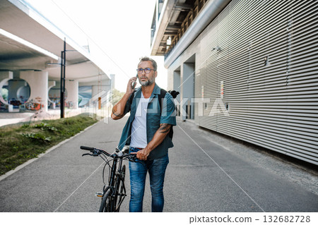 Male cyclist making phone call, standing by his bike. Male cyclist making phone call, standing by his bike. 132682728