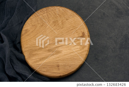 Empty round brown wooden cutting board on a black background Empty round brown wooden cutting board on a black background 132683426