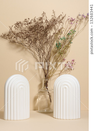 A vase with dried flowers and two white fluted arches on a beige background 132683441