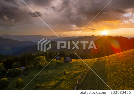 Hikers shelter on mountainside. Beautiful nature landscape. Aerial view of colorful sunset in wild mountains. Dark pine forest illuminated with bright setting sun 132683490