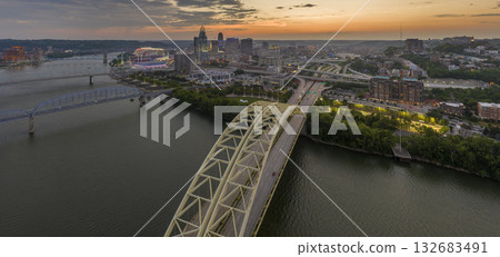 Highway traffic with driving cars on bridge in downtown district of Cincinnati city in Ohio, USA. American city skyline with brightly illuminated high commercial buildings at night Highway traffic with driving cars on bridge in downtown district of Cincinnati city in Ohio, USA. American city skyline with brightly illuminated high commercial buildings at night 132683491