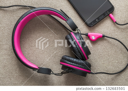 Headphone connected to cellphone isolated on light cloth flat copy space background. Modern technology, trendy entertainment, gadget design and accessories concept. 132683501
