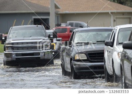 Flooded Florida road with evacuating cars and surrounded with water houses in suburban residential area. Consequences of hurricane natural disaster Flooded Florida road with evacuating cars and surrounded with water houses in suburban residential area. Consequences of hurricane natural disaster 132683553