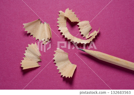 Close-up of wooden pencil shavings and a pencil lying on a purple background. Close-up of wooden pencil shavings and a pencil lying on a purple background. 132683563