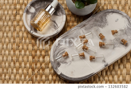 A bottle with a pipette surrounded by small empty bottles with corks. The objects are arranged on a marble tray, a wicker background A bottle with a pipette surrounded by small empty bottles with corks. The objects are arranged on a marble tray, a wicker background 132683582