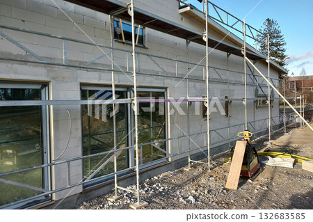 Facade of building made from white blocks with big windows under construction works. Facade of building made from white blocks with big windows under construction works. 132683585