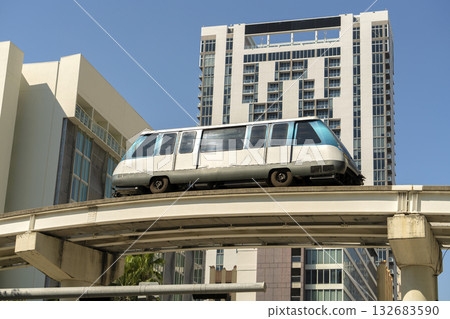 Elevated train for public transportation in Miami city downtown district in Florida USA. Metrorail train car on railroad over street traffic between skyscraper buildings in modern American urban area 132683590