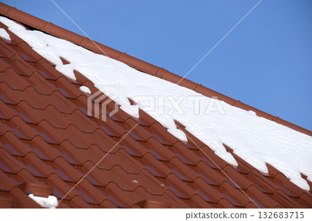 Closeup of house roof top covered with snow in cold winter. Tiled covering of building in wintertime weather Closeup of house roof top covered with snow in cold winter. Tiled covering of building in wintertime weather 132683715