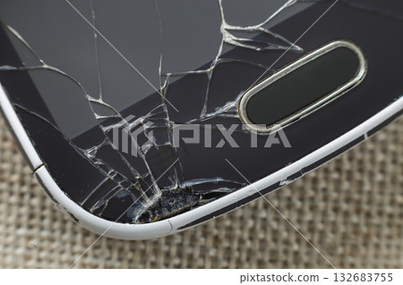 Close-up detail of black old cellphone with cracked screen on light cloth background. Gadget repair and maintenance concept. Close-up detail of black old cellphone with cracked screen on light cloth background. Gadget repair and maintenance concept. 132683755