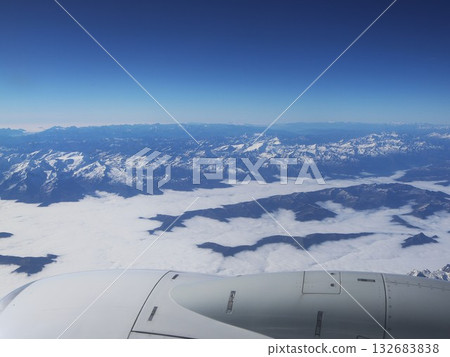 Aerial View Over Snowy Mountain Range With Clouds From An Airplane Window Aerial View Over Snowy Mountain Range With Clouds From An Airplane Window 132683838