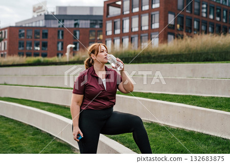 Sporty woman resting, drinking water after training. 132683875