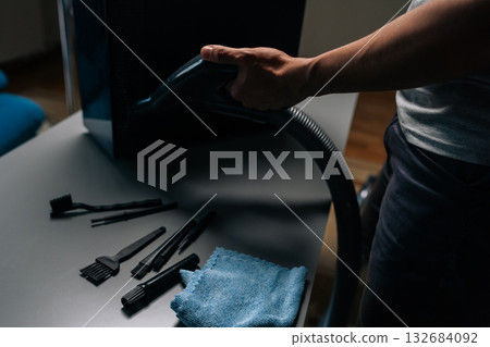 Computer technician cleaning computer case with vacuum cleaner, different brushes and microfiber cloth on table, performing maintenance and removing dust in dark workshop, close-up. Computer technician cleaning computer case with vacuum cleaner, different brushes and microfiber cloth on table, performing maintenance and removing dust in dark workshop, close-up. 132684092