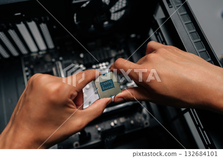 Close-up hands of technician inserting processor into desktop motherboard during computer hardware upgrade or repair process at dark workshop. Concept of desktop PC maintenance and service. 132684101