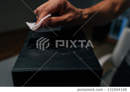 Close-up of technician hand cleaning dust and grime from computer case with tissue, ensuring optimal performance and hygiene. Concept of importance of regular cleaning for optimal performance. 132684106