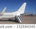 White Commercial Airplane On Ground With Boarding Stairs At Airport, City Skyline In Background 132684340