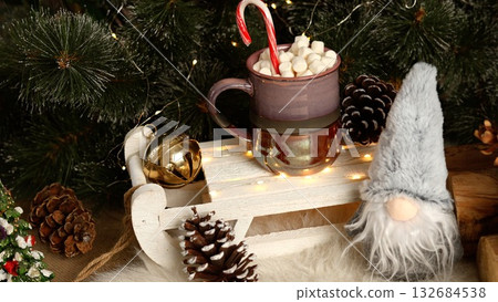 Holiday clay mug of hot chocolate with marshmallows and candy cane, paired with pinecones, golden accents, red berries, and green pines, showcasing rustic Christmas charm. 132684538