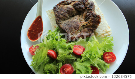 Grilled meat served with greens and pitta bread on white plate at the restaurant Grilled meat served with greens and pitta bread on white plate at the restaurant 132684575