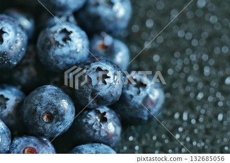 Delicious fresh blueberries glisten with water droplets, beautifully highlighting their vibrant color and texture against a dark, bokeh background. Concept of healthy eating, fresh produce, and macro  132685056