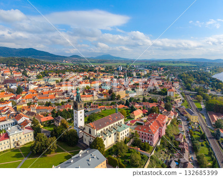 Aerial view captures St. Stephen's Cathedral standing tall in Litomerice, Czechia. Surrounding buildings and lush landscape create a beautiful scene during clear weather. Aerial view captures St. Stephen's Cathedral standing tall in Litomerice, Czechia. Surrounding buildings and lush landscape create a beautiful scene during clear weather. 132685399