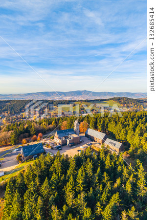 Kralovka Lookout Tower rises above vibrant autumn foliage in the Jizera Mountains. Visitors enjoy panoramic views of the surrounding landscape, showcasing the colors of fall. Kralovka Lookout Tower rises above vibrant autumn foliage in the Jizera Mountains. Visitors enjoy panoramic views of the surrounding landscape, showcasing the colors of fall. 132685414