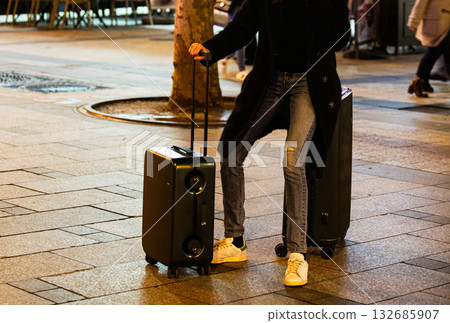 A modern traveler rests on their luggage on a city street. Concept for the journey, a pause, and the modern urban lifestyle. A modern traveler rests on their luggage on a city street. Concept for the journey, a pause, and the modern urban lifestyle. 132685907