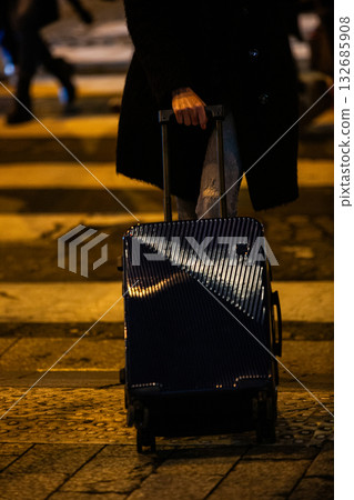 A traveler with luggage on a city street at night. 132685908