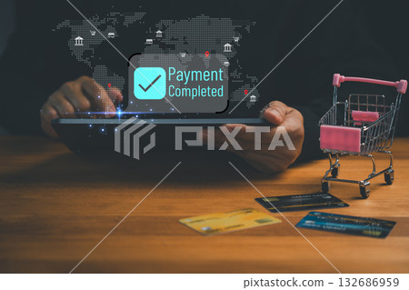 Online payment success concept with a person holding a tablet showing Payment Completed on screen. Credit cards and a shopping cart symbolize e-commerce, digital banking and secure transactions. Online payment success concept with a person holding a tablet showing Payment Completed on screen. Credit cards and a shopping cart symbolize e-commerce, digital banking and secure transactions. 132686959