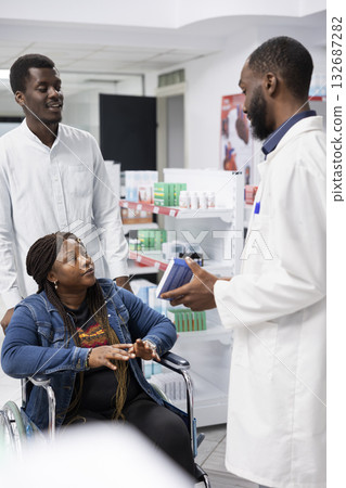 Pharmacist counseling a customer with disability on treatment options, discussing about medication dosage to support patient health. Professional medical staff showing drugstore pills. Pharmacist counseling a customer with disability on treatment options, discussing about medication dosage to support patient health. Professional medical staff showing drugstore pills. 132687282