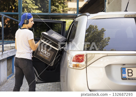 Female courier arriving at drop off address by car and delivering meal, taking out backpack to bring fast food to a client at the front door. Takeaway delivery service from a restaurant. 132687293