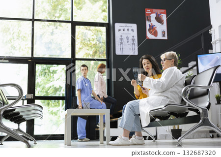 Female asian patient listens as a nurse explains X ray results during routine checkup. Medic at consultation gives accurate diagnosis and imaging interpretation, professional care. Female asian patient listens as a nurse explains X ray results during routine checkup. Medic at consultation gives accurate diagnosis and imaging interpretation, professional care. 132687320